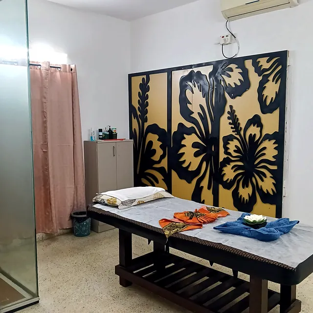 Treatment room with a hibiscus wall panel, a dark wood massage bed, folded towels and an attached shower