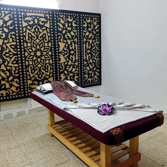 Massage bed with a silk runner and a purple lotus beneath an ornate black and gold Thai lattice panel