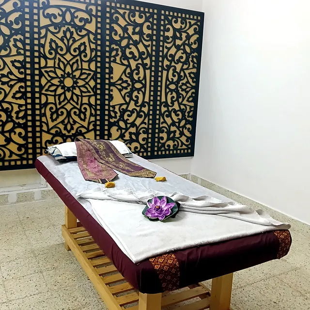 Treatment room with an ornate Thai lattice wall panel and a massage bed laid with fresh towels