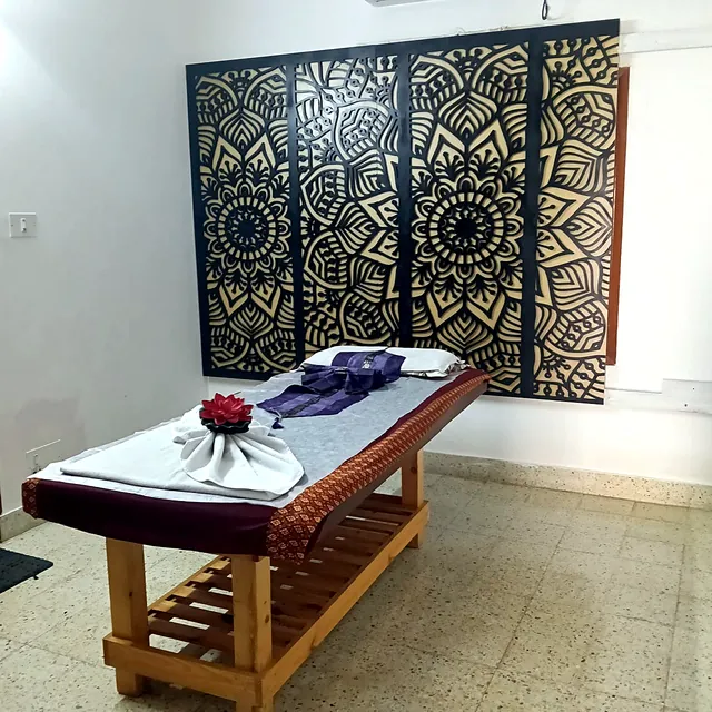Massage bed dressed with a Thai runner and a towel lotus in front of a black and gold mandala screen