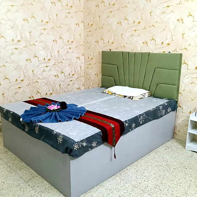 Wide massage bed with a green upholstered headboard, a Thai runner and a towel fan with a lotus