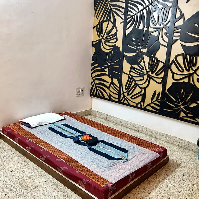 Traditional Thai massage floor mattress with a silk runner and a flower, beside a tropical leaf wall panel